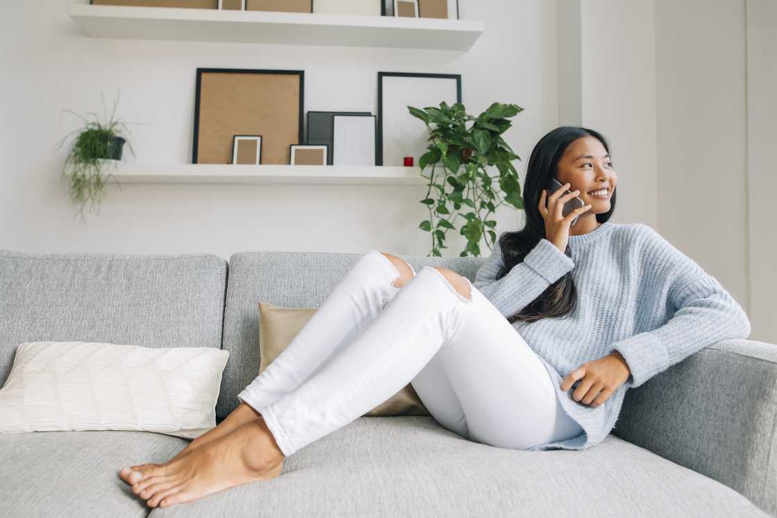 A young woman sitting on couch at home telephoning with a cell phone