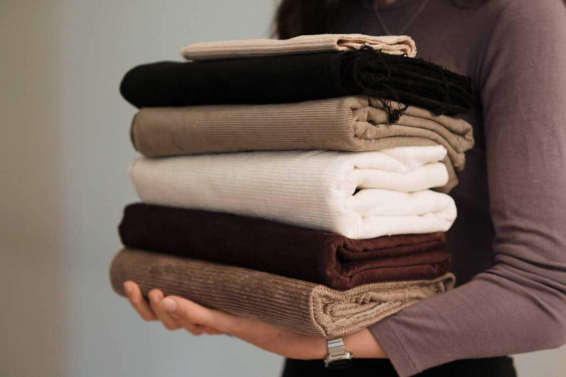 Person holding a neatly stacked pile of folded clothes. Person holding a neatly stacked pile of folded clothes.