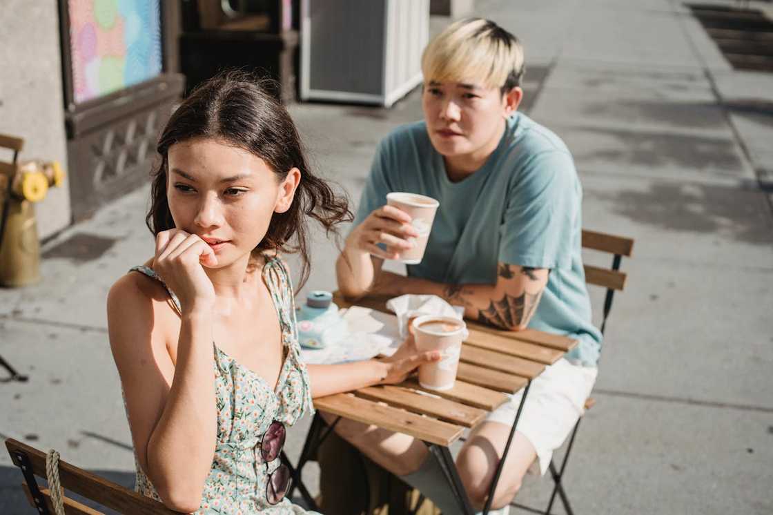A woman sitting at an outdoor café table looks away thoughtfully.