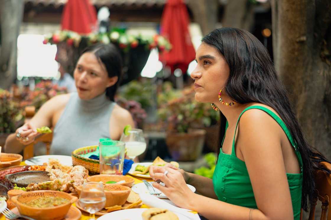 Two women sit at an outdoor table eating and talking over a meal. Two women sit at an outdoor table eating and talking over a meal.