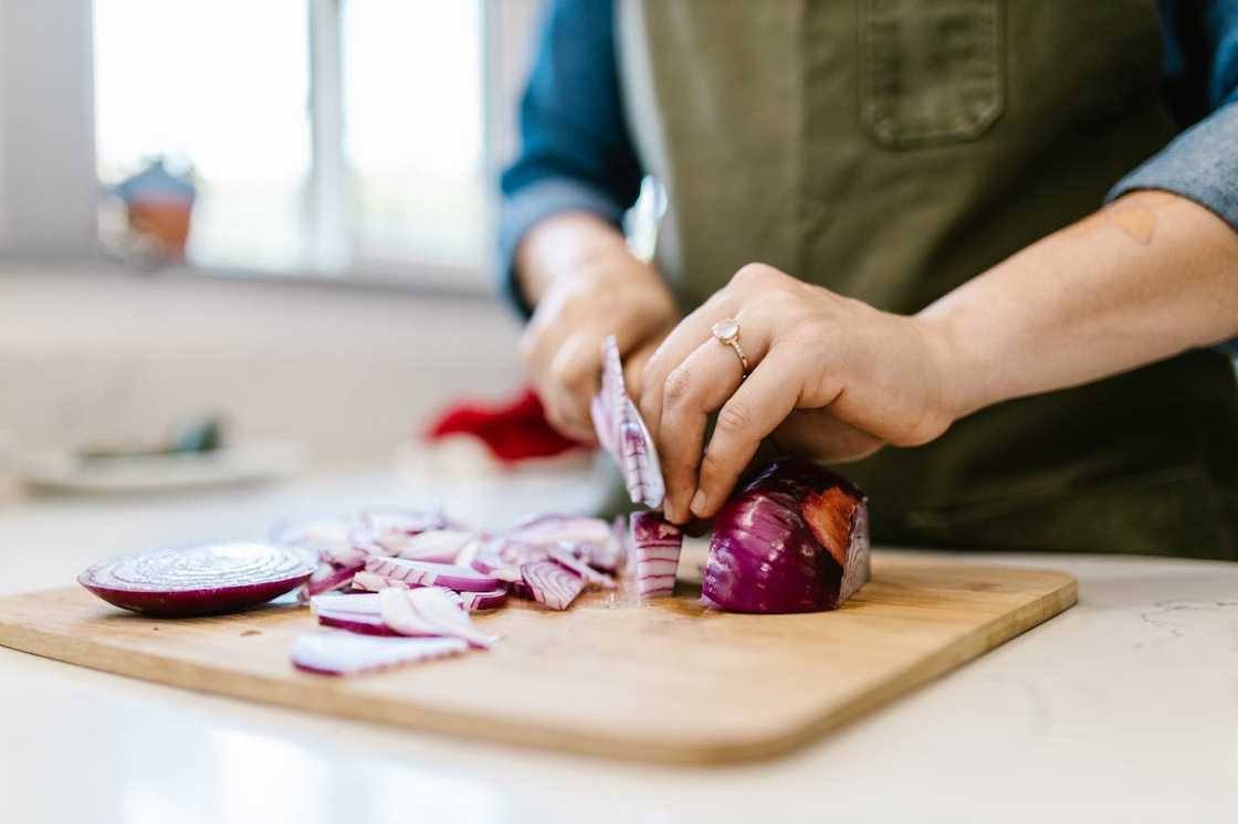 A person slices a red onion on a cutting board. A person slices a red onion on a cutting board.