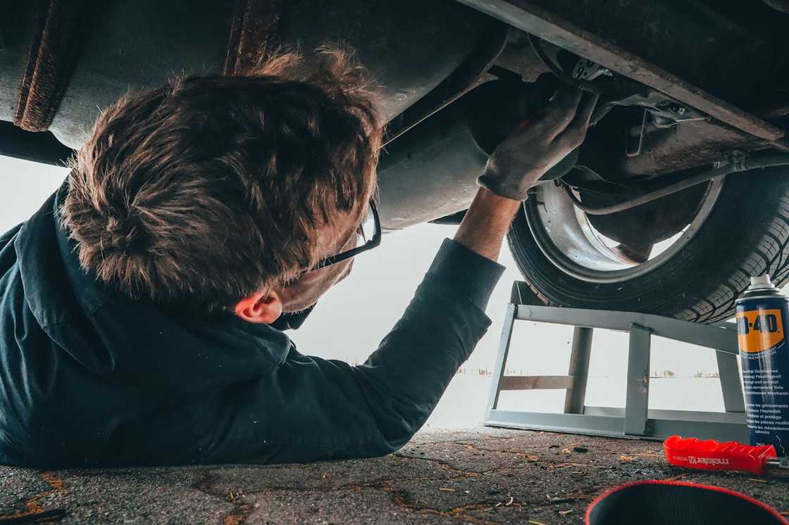 A mechanic inspects the underside of a car with tools.