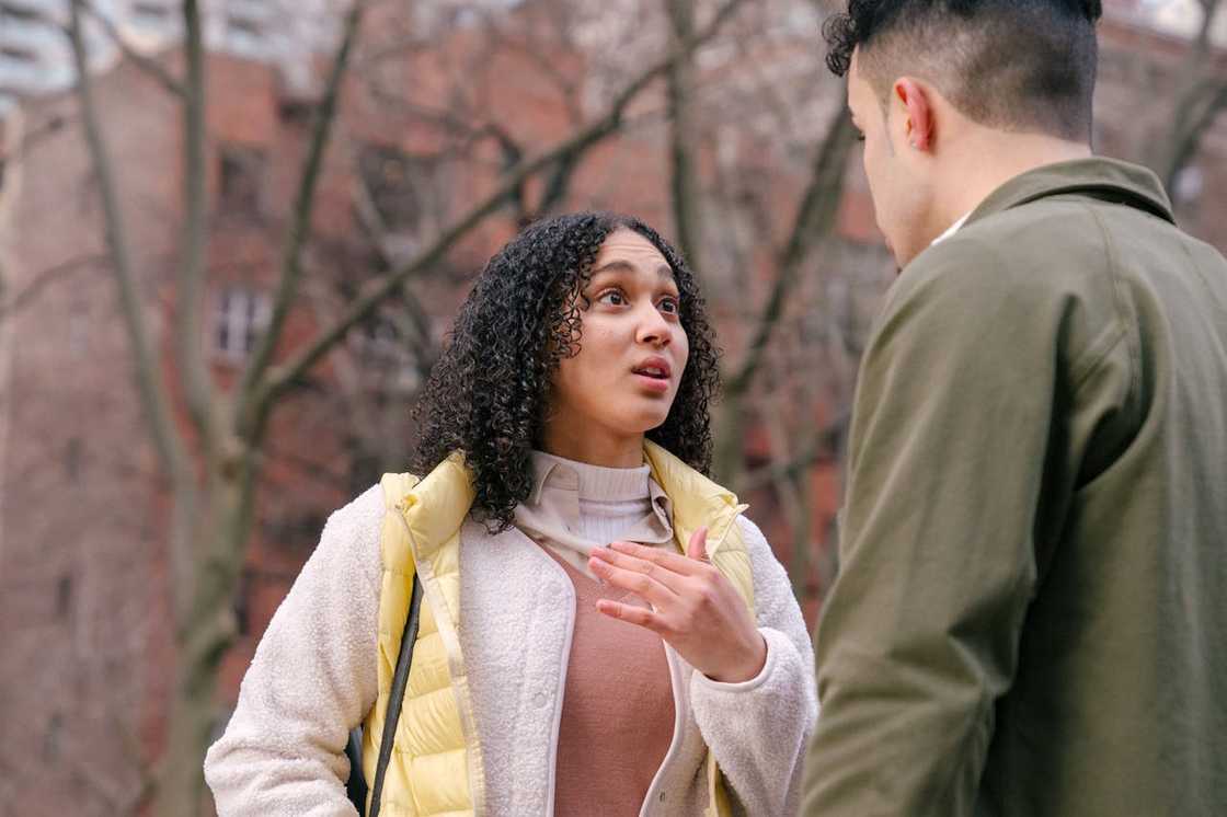 A woman gestures while speaking to a man during a tense conversation outdoors. A woman gestures while speaking to a man during a tense conversation outdoors.