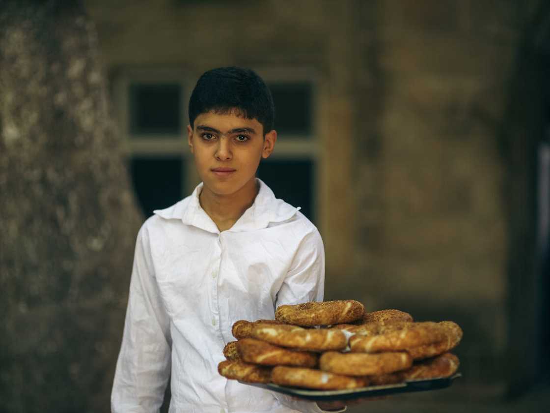 A teenage boy carrying a tray of bread rolls. A teenage boy carrying a tray of bread rolls.
