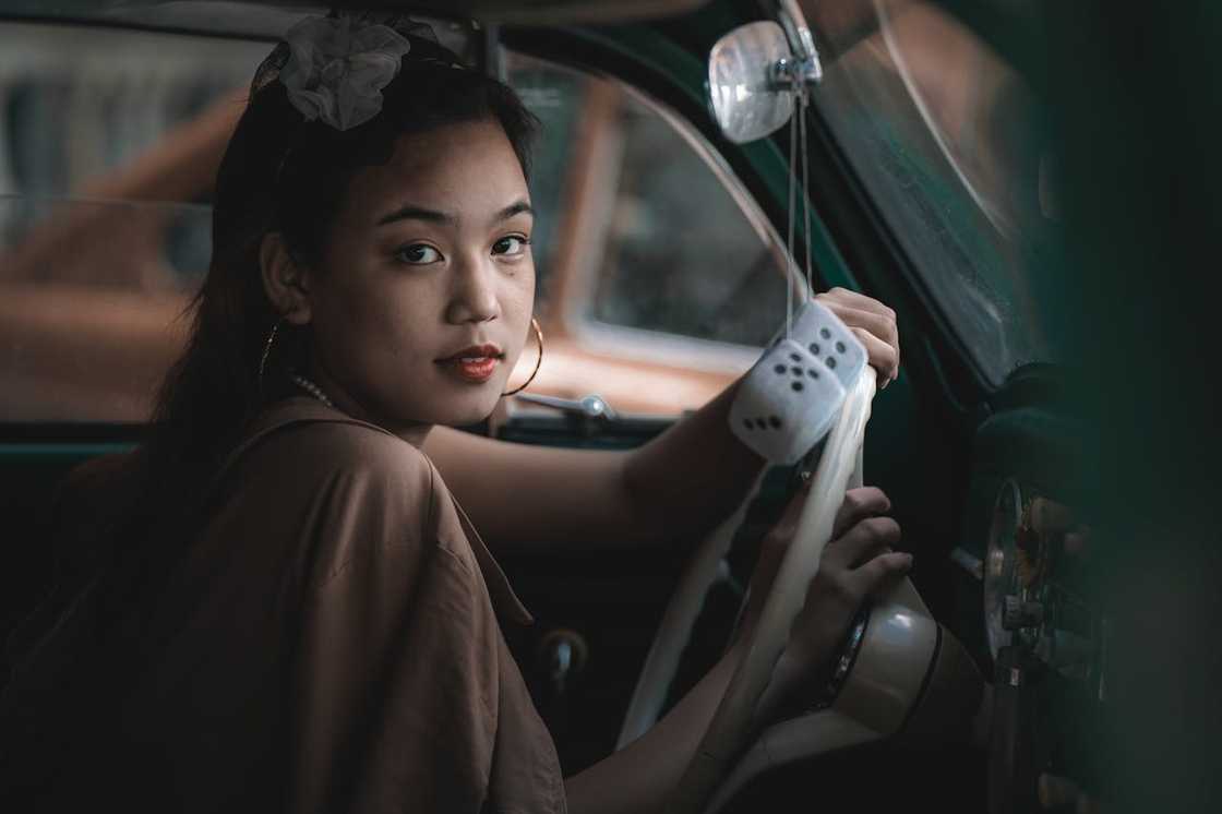 A woman sits in a van holding the steering wheel and looking back toward the camera.