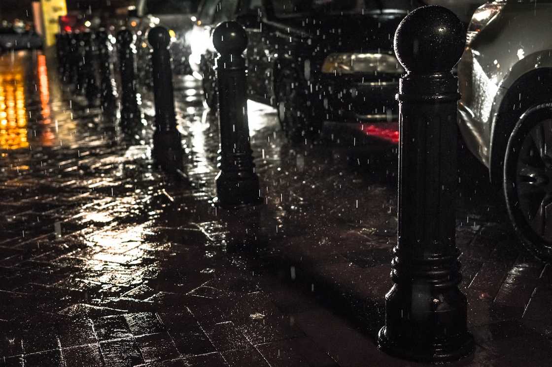 Rain-soaked street with parked cars and reflective pavement at night. Rain-soaked street with parked cars and reflective pavement at night.