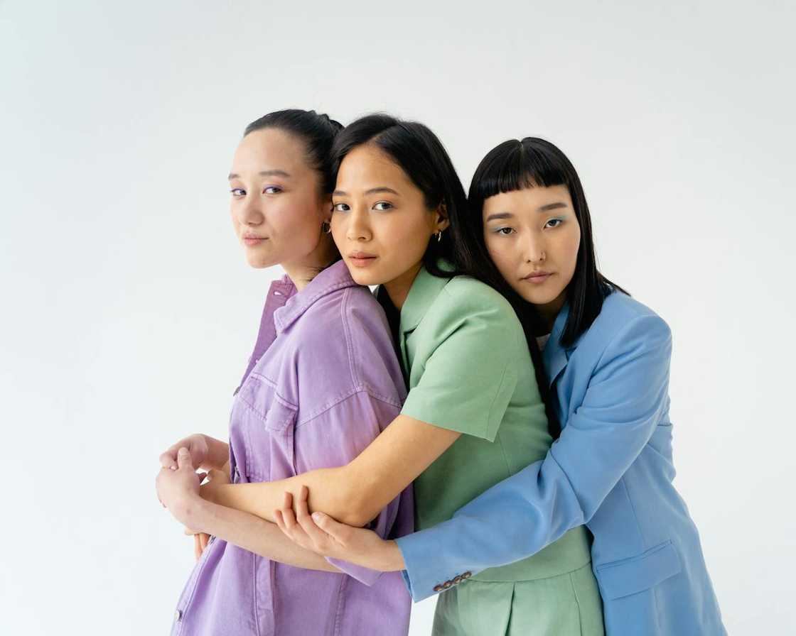 Three women stand closely together, embracing, wearing pastel outfits. Three women stand closely together, embracing, wearing pastel outfits.