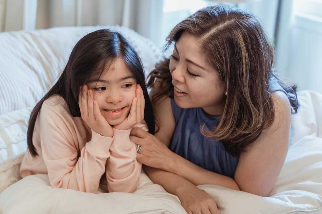 A woman and a young girl sitting on the bed.