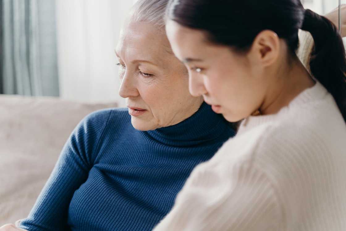 An older woman and a younger woman sit closely together.