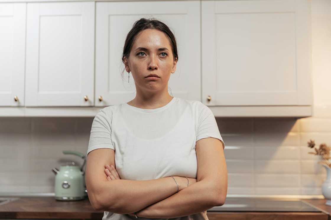 A woman with her arms crossed looks upset in the kitchen.