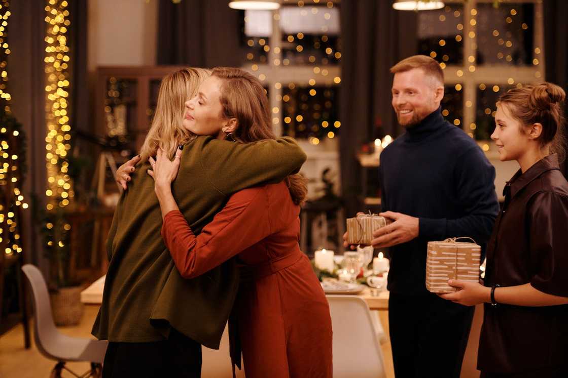Family hugging and exchanging gifts at a warmly lit dinner gathering.