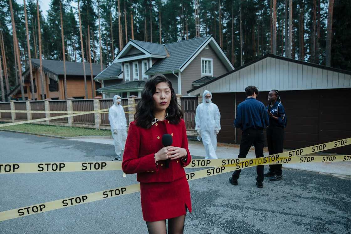 Crime scene outside a house with a reporter, forensic team, and police near yellow tape. Crime scene outside a house with a reporter, forensic team, and police near yellow tape.