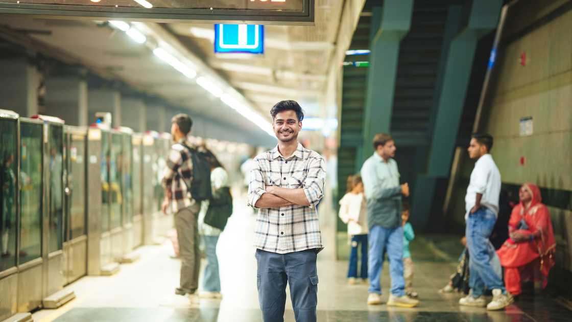 A young man stands on a train platform with his hands folded. A young man stands on a train platform with his hands folded.