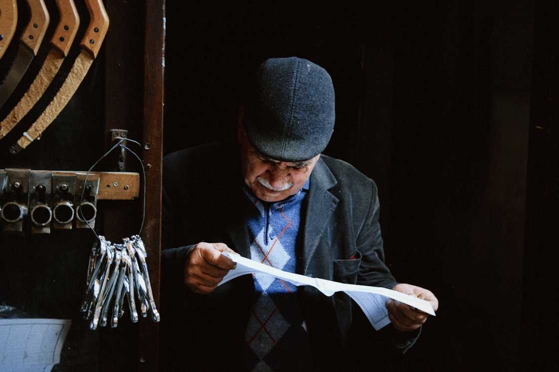 An elderly man reads a document inside a small workshop.