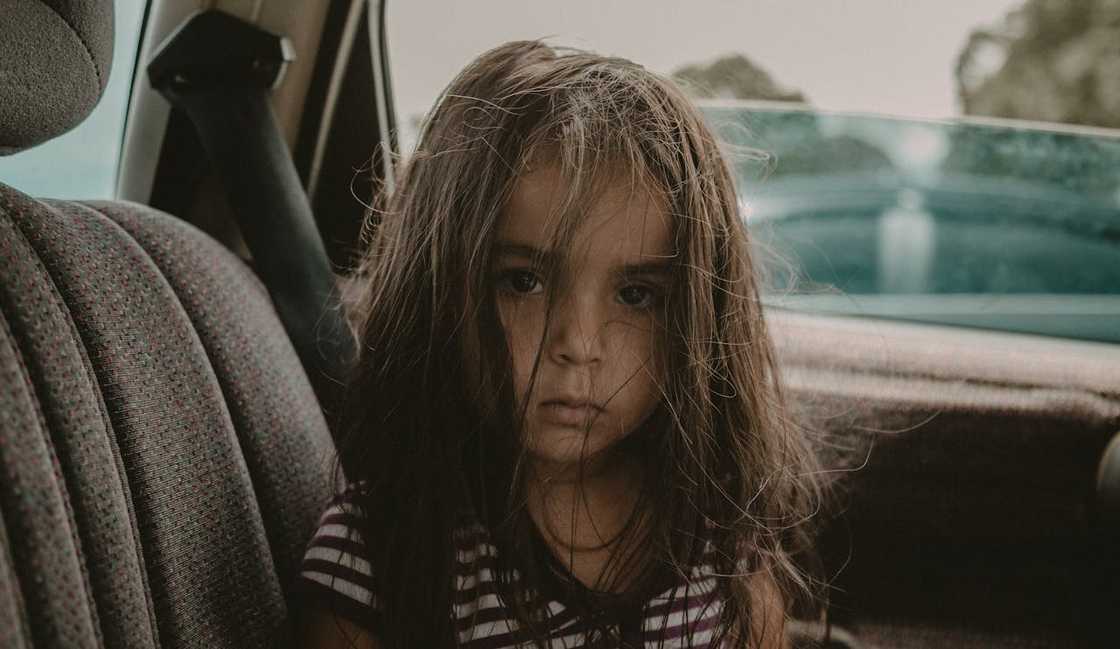 A young child sitting quietly in the back seat of a car.