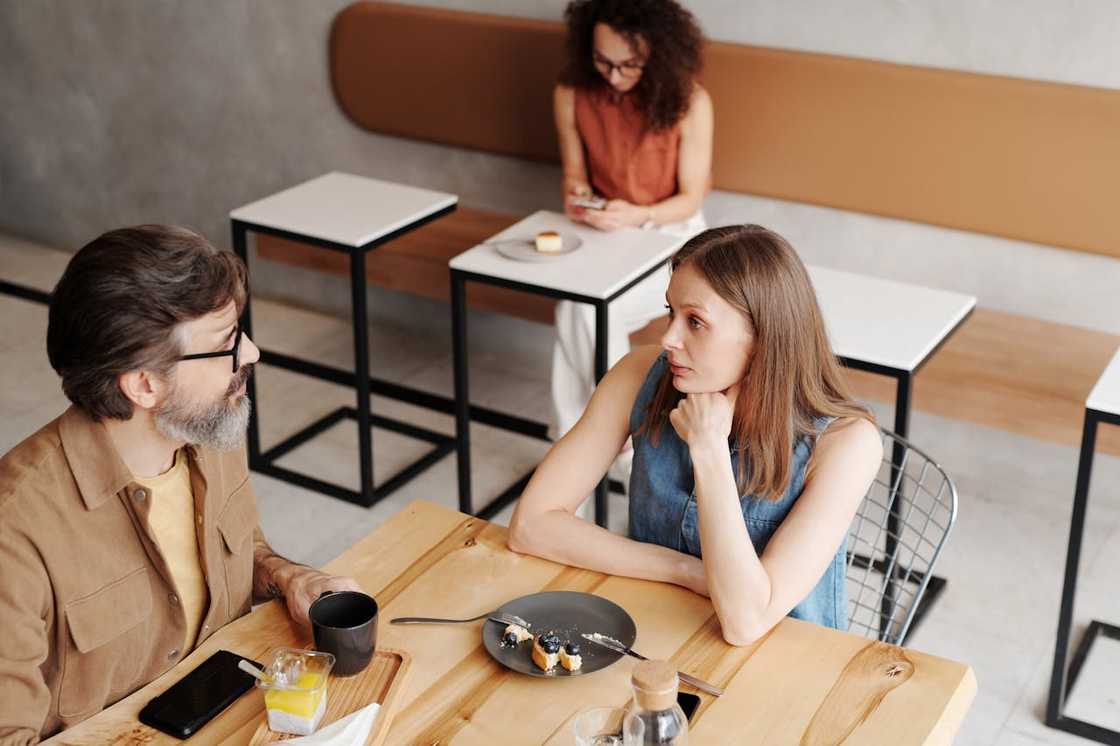 A man and a woman sit across from each other at a café table. A man and a woman sit across from each other at a café table.