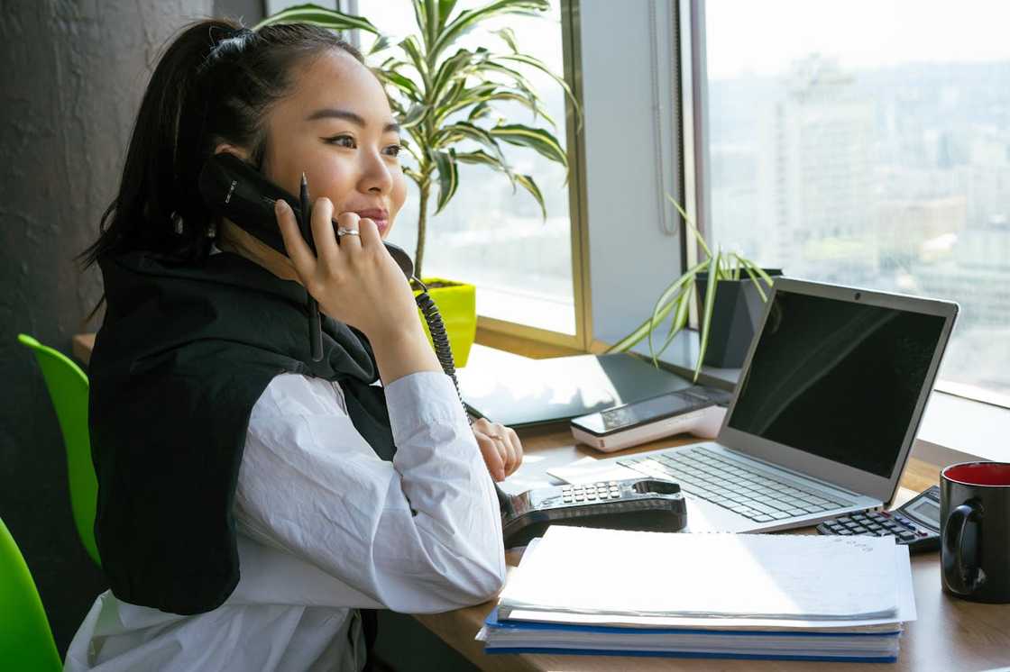 A smiling woman talking on the phone while working on a laptop. A smiling woman talking on the phone while working on a laptop.