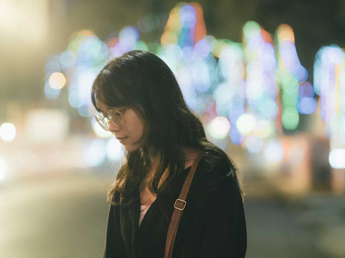 A woman walks outdoors at night, wearing a dark outfit with a brown shoulder strap. A woman walks outdoors at night, wearing a dark outfit with a brown shoulder strap.