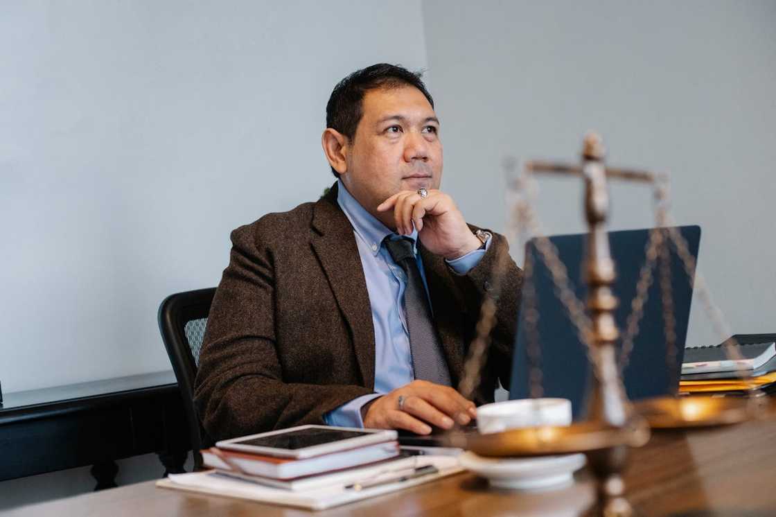 A lawyer in a suit sitting at a desk, resting his chin on his hand and thinking.
