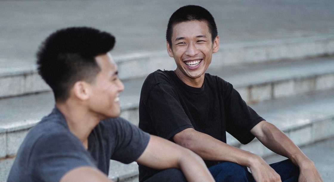 Two friends sit on outdoor steps, smiling and talking together.