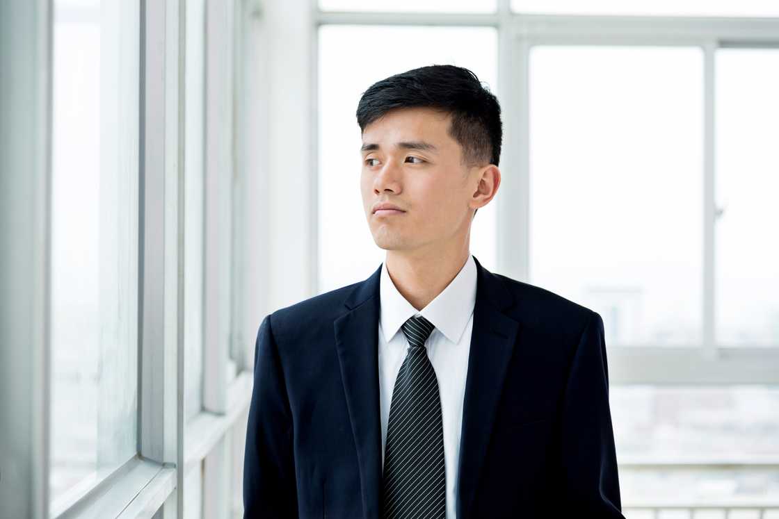 A man standing near a window inside an office A man standing near a window inside an office