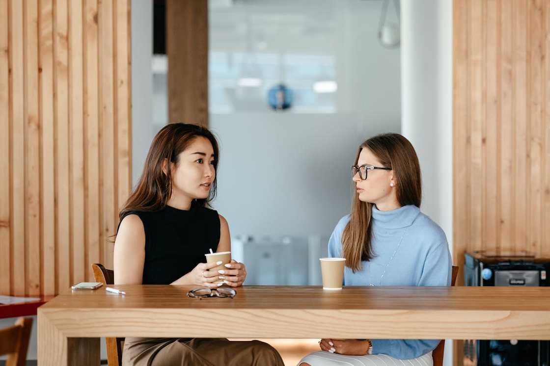 Two women sit across a wooden table in a cafe. Two women sit across a wooden table in a cafe.