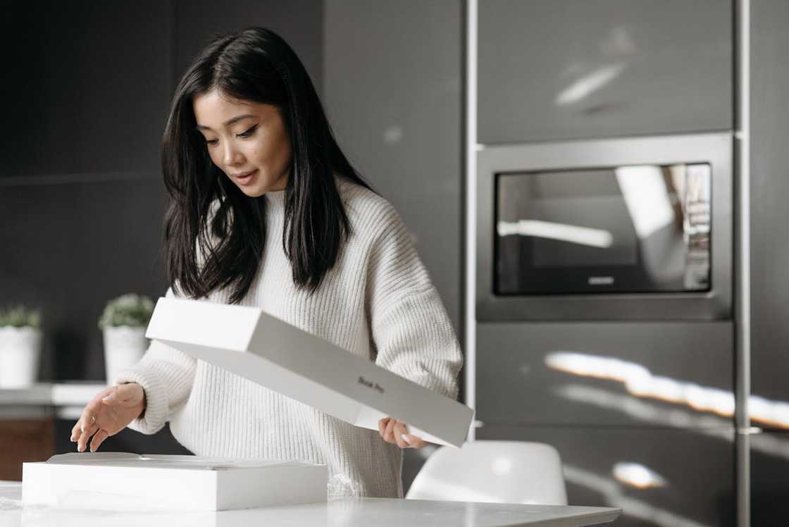 A woman in a white knitted sweater unpacks a white box.