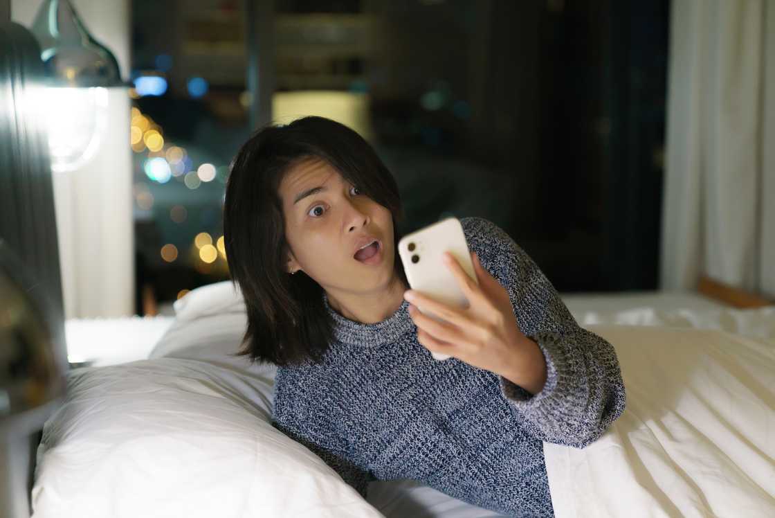 A lady reads a shocking text in bed