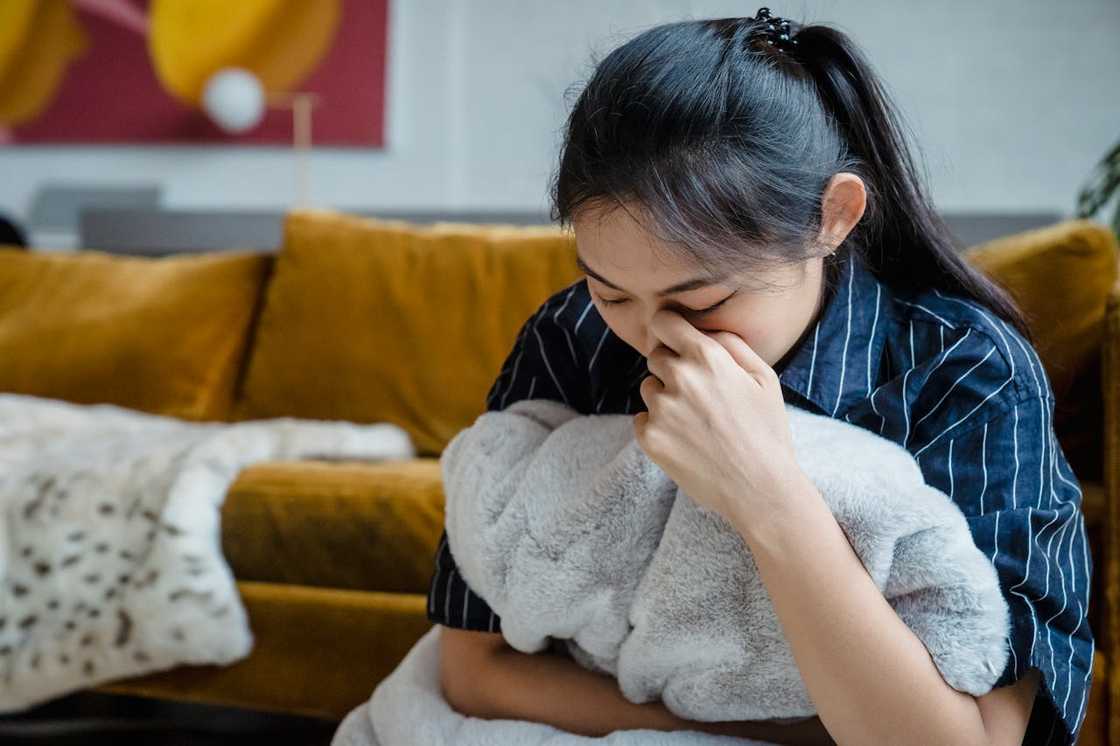 A woman sitting on a couch, crying while holding a pillow.
