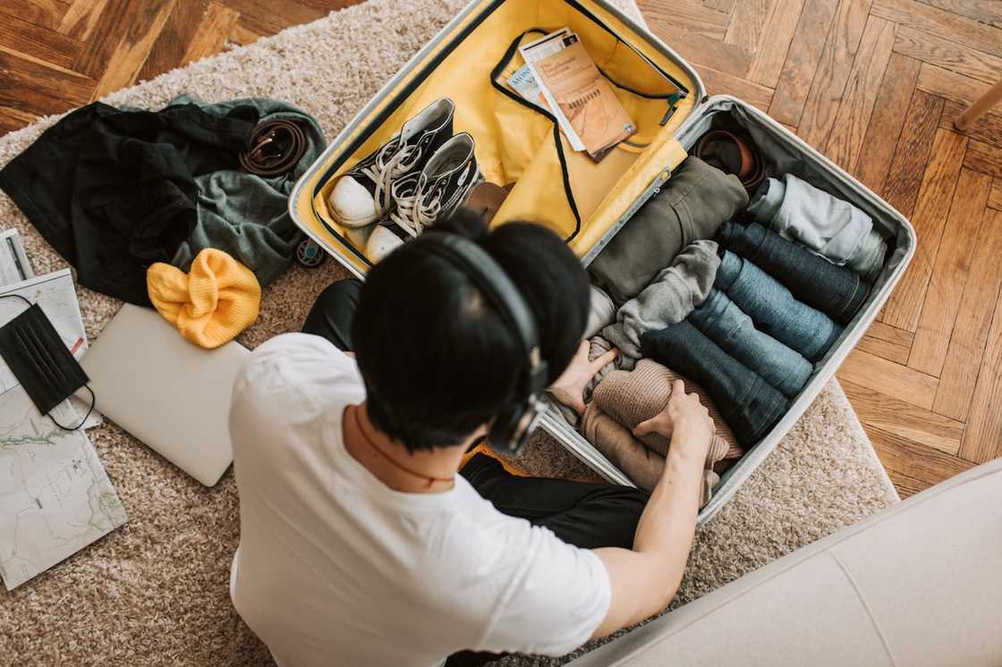 A young man packs a suitcase while listening to his headphones. A young man packs a suitcase while listening to his headphones.
