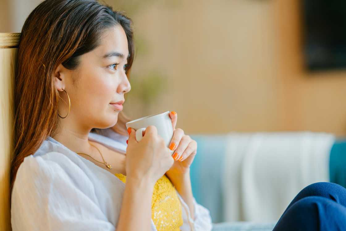 A young woman sitting on a the couch drinking tea