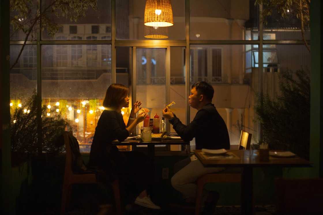 A couple is seated at a restaurant table at night, talking while eating.