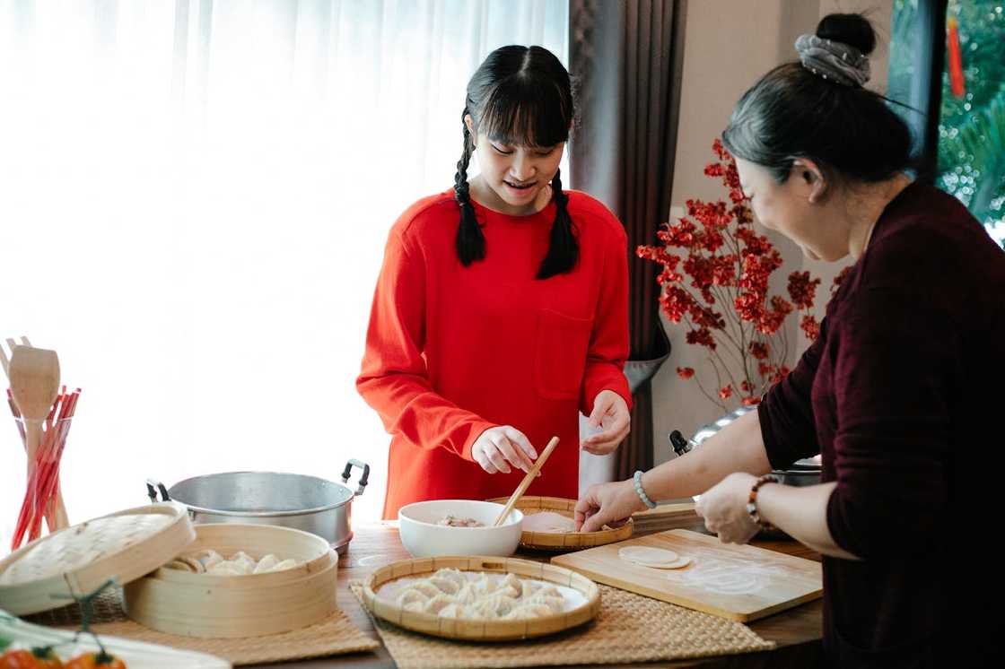 An Asian grandmother with her teenage granddaughter cooks at home.