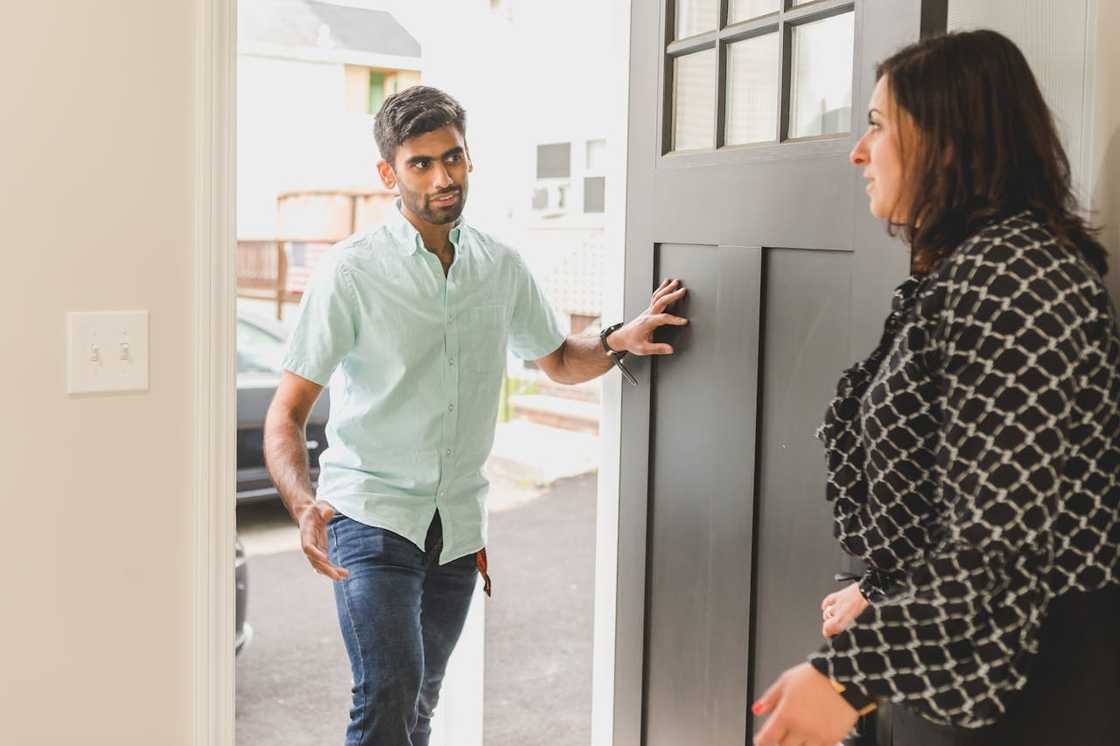A man stands at a doorway speaking to a woman. A man stands at a doorway speaking to a woman.