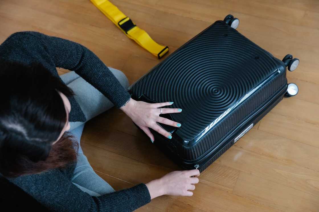 A woman sits on the floor closing a suitcase while packing. A woman sits on the floor closing a suitcase while packing.