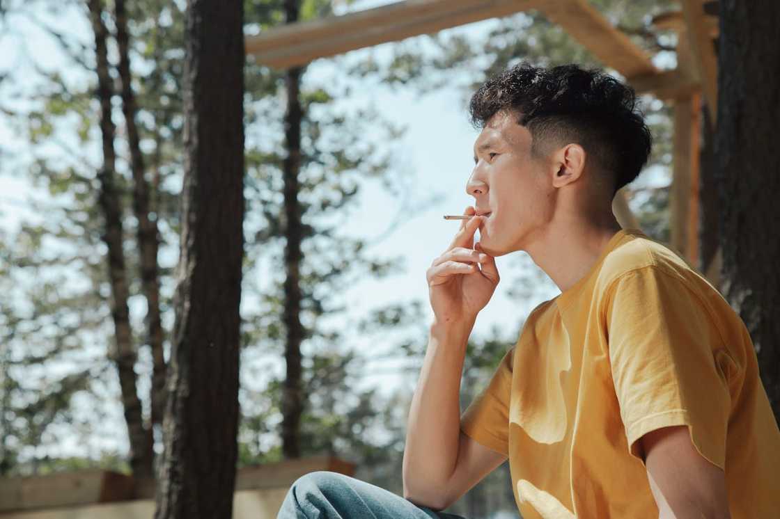 A man smokes outdoors, looking thoughtful.