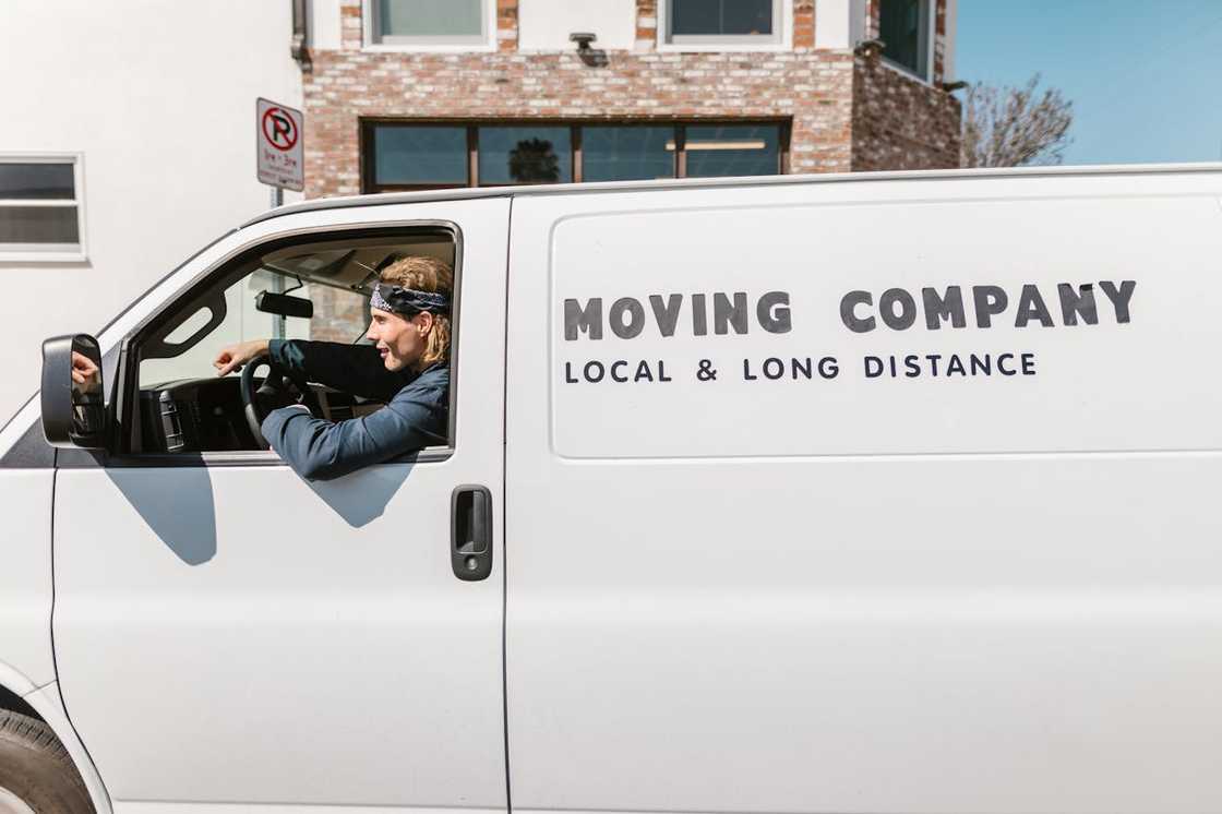A driver leans out of a moving van marked "Moving Company." A driver leans out of a moving van marked "Moving Company."