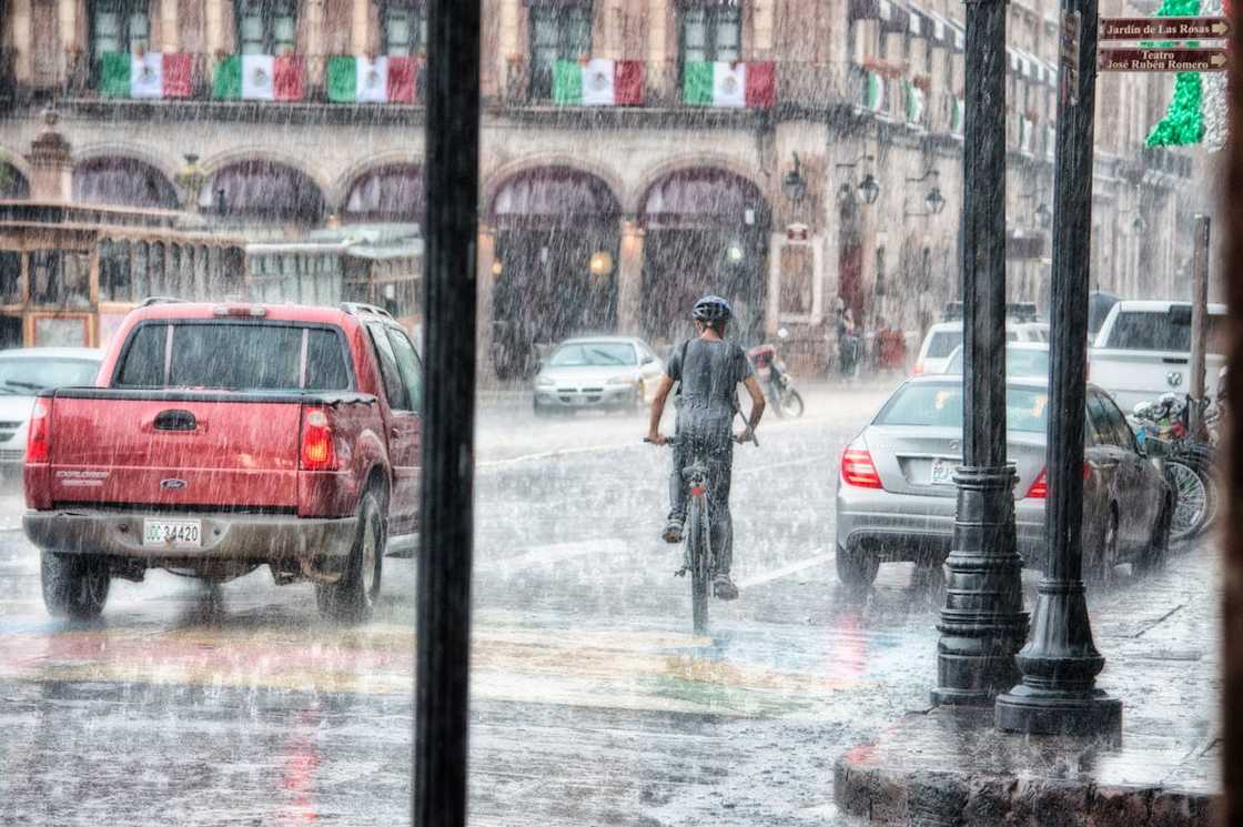 A cyclist riding through heavy rain on a busy city street.