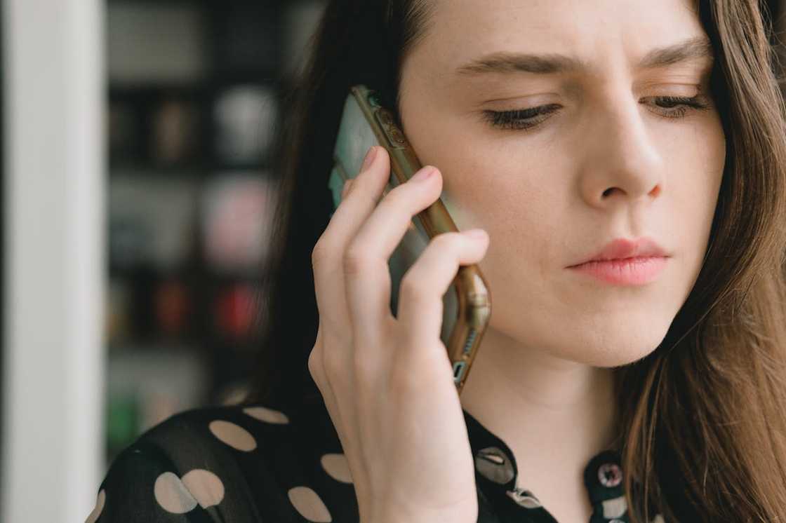 A woman holds a phone to her ear, listening quietly with a serious expression.