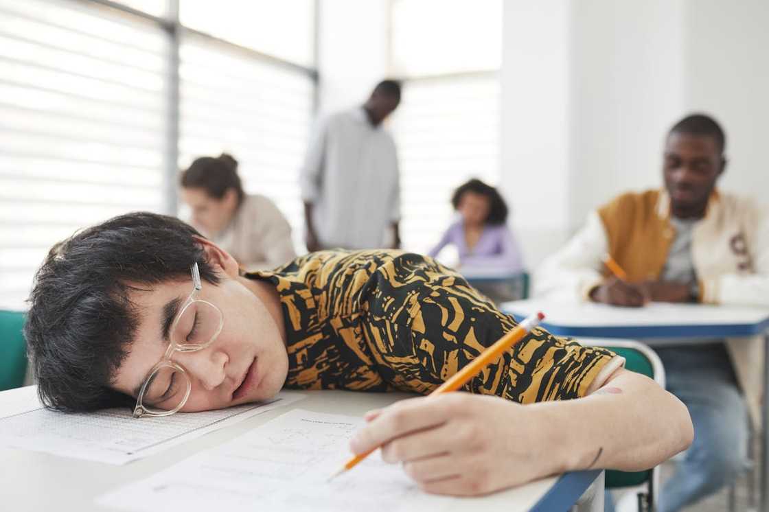 A student is asleep on a desk during a classroom test. A student is asleep on a desk during a classroom test.