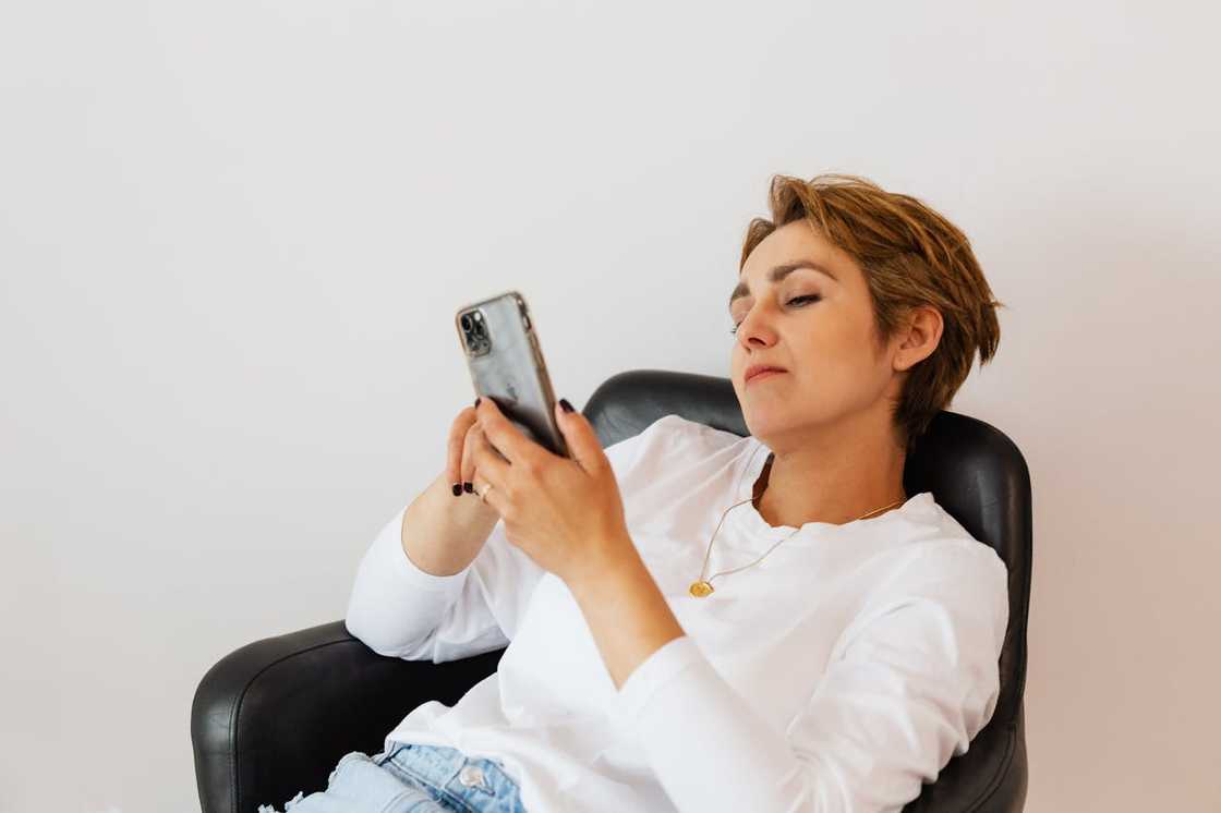 A woman reclines in a chair while looking at her phone with a calm, focused expression.