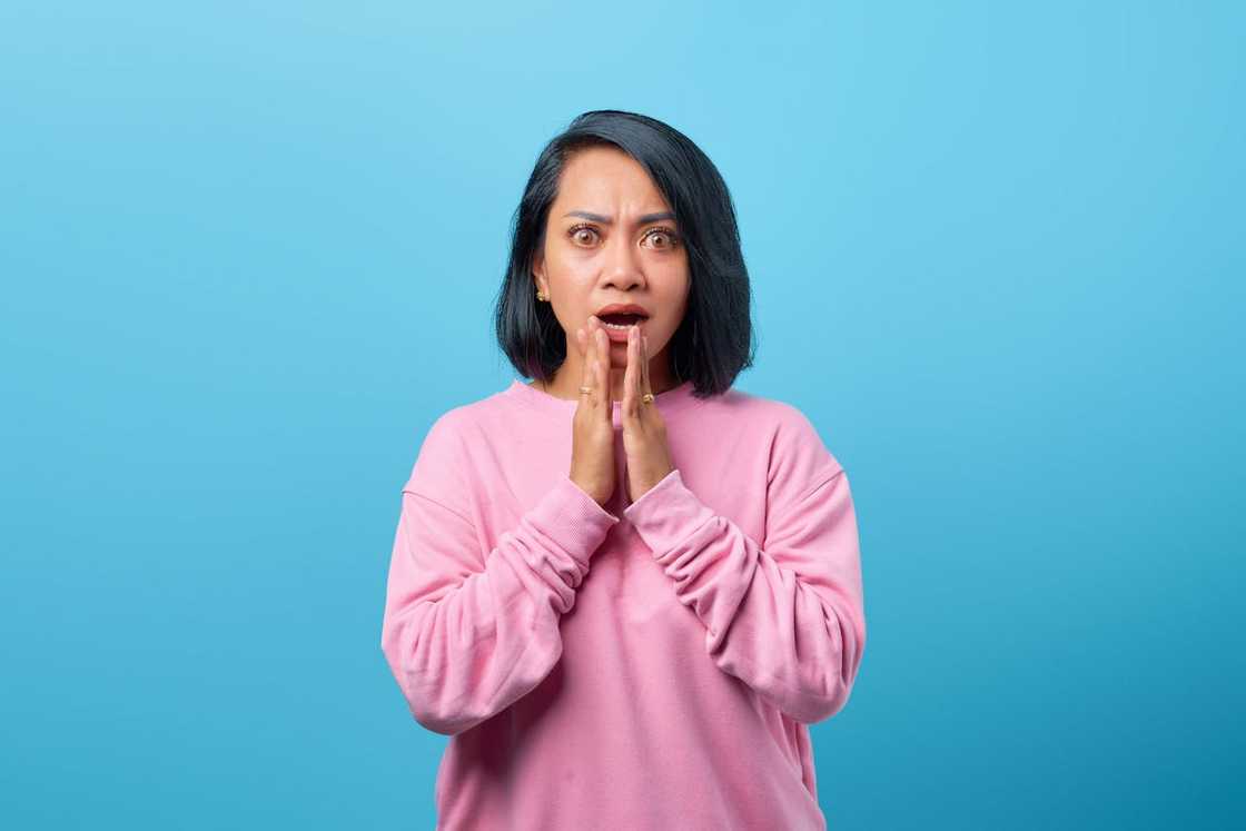 A woman looking shocked with her hands to her face.