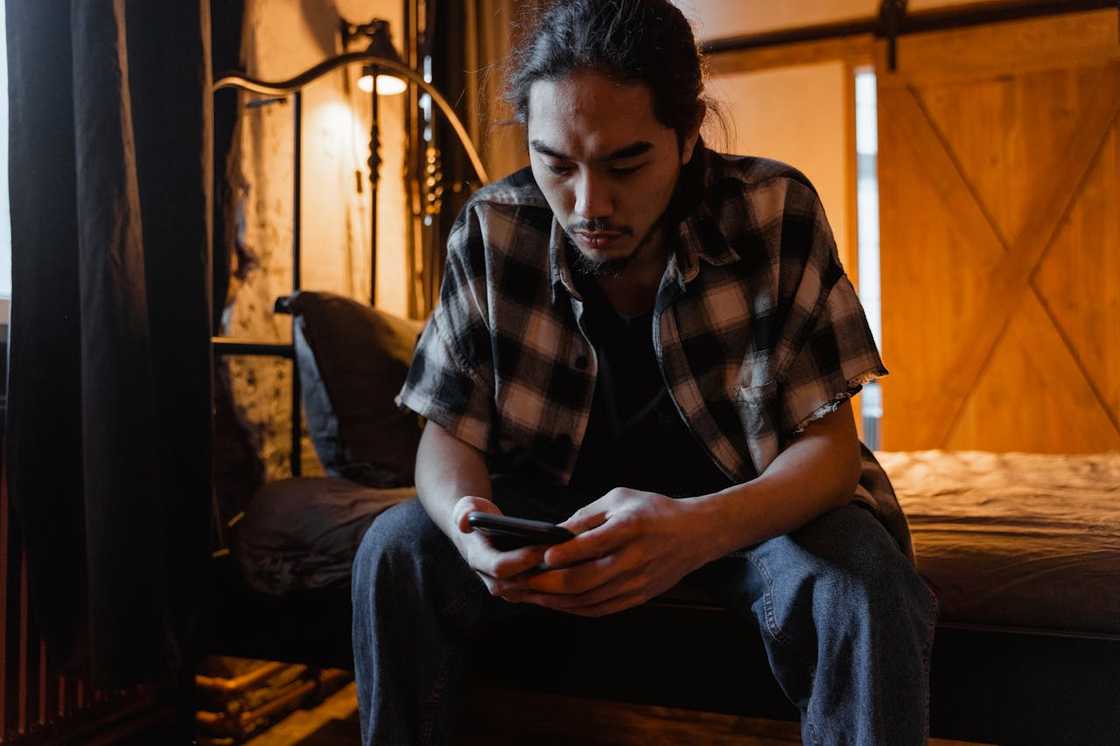 A man sitting alone in his room staring at a his phone. A man sitting alone in his room staring at a his phone.
