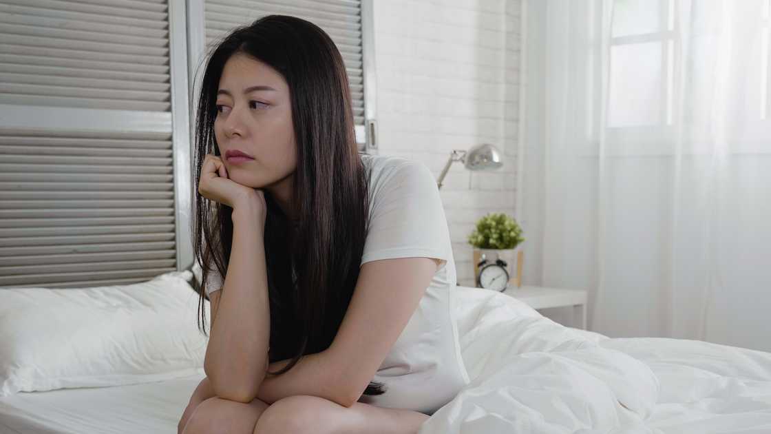 A sad Asian woman sitting on bed looking away A sad Asian woman sitting on bed looking away