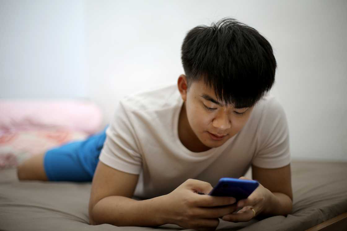A young man using his smartphone in his bedroom.