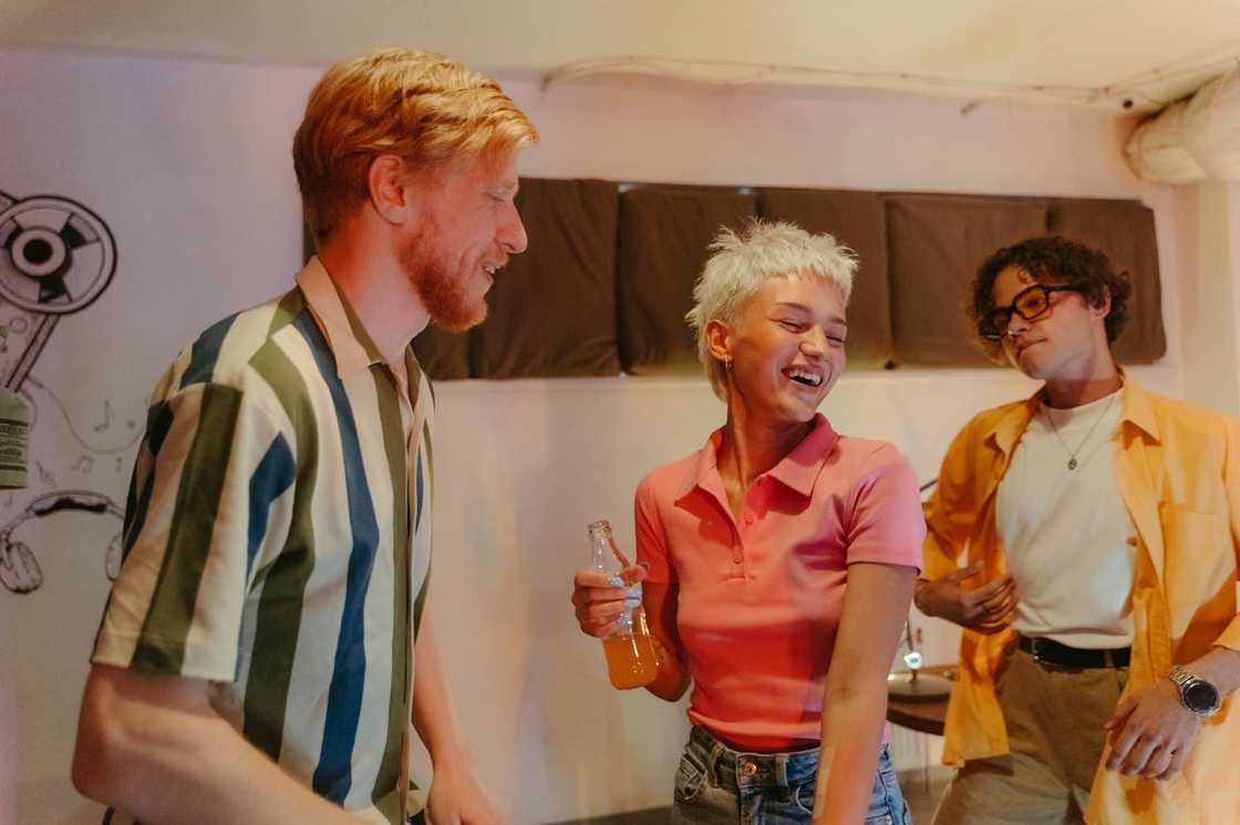 Friends laughing and dancing indoors, one holding a drink.