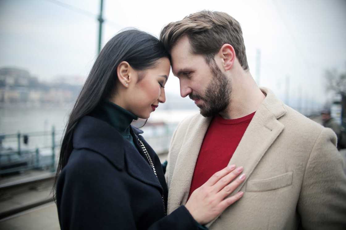 A couple stands close outdoors, foreheads touching, sharing an intimate and emotional moment. A couple stands close outdoors, foreheads touching, sharing an intimate and emotional moment.