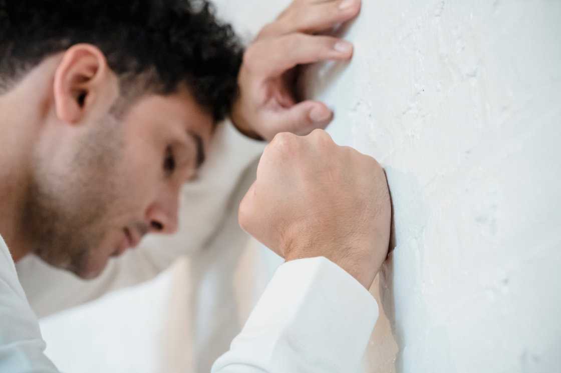 A man leans his head against a brick wall, appearing stressed.