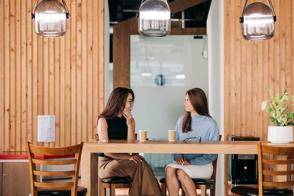Two friends talk at a table while having coffee in a cafe. Two friends talk at a table while having coffee in a cafe.