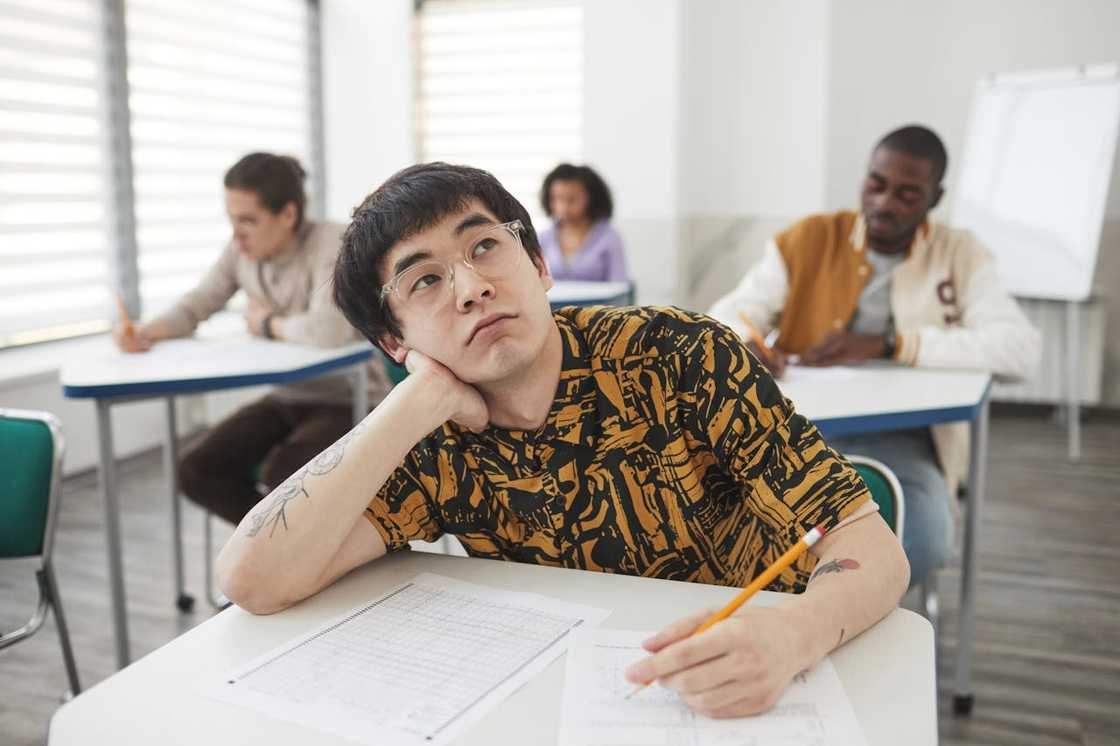 A student sits at a desk while classmates work behind him.